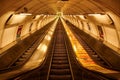 Escalator illuminated in a golden hue, descending through a subway tunnel in Prague