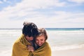 Escaping the cold ocean breeze. an affectionate young couple wrapped in a blanket on the beach. Royalty Free Stock Photo