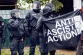 Black uniformed policemen with helmets and lowered visors stand behind demonstrators of Anti Fascist Action holding up a banner Royalty Free Stock Photo