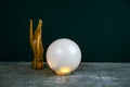 esoteric still life with a ball of predictions and wooden female hand on concrete table against black wall