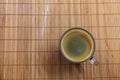 Espresso coffee with golden fine-bubbled crema seen from above in a crystal clear cup on bamboo plate holder.