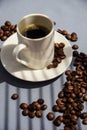 Espresso in a white mug on a white saucer next to coffee beans on a gray background. Royalty Free Stock Photo