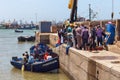 ESSAOUIRA, MOROCCO - JUNE 09, 2017: Unknown people on the pier in Essaouira harbor near the blue fishing wooden boat in the water Royalty Free Stock Photo