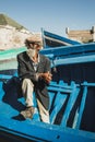 Old senior fisherman on blue wooden boat in Essaouira harbor. Moroccan people.