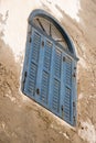 ngled faded blue shuttered window with fanlight set in a peeling plaster wall - dutch tilt