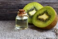 Essential kiwi seed oil in a glass jar with fresh halved kiwifruit on old wooden background. Aromatherapy,spa,beauty treatment and