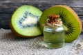 Essential kiwi seed oil in a glass jar with fresh halved kiwifruit on old wooden background. Aromatherapy,spa,beauty treatment and