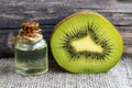 Essential kiwi seed oil in a glass jar with fresh halved kiwifruit on old wooden background. Aromatherapy,spa,beauty treatment and