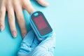 An essential medical device for hypoxia. A hand in a medical glove holds a pulse oximeter on a blue background