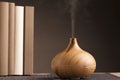 Essential oil air freshener on wood with steam, shelf with books, brown background.