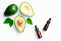 Essential oils bottles and avocado with green leaves on white background. Flat lay, top view. Aromatherapy massage oil, avocado