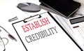 ESTABLISH CREDIBILITY text on paper clipboard with chart and notebook on withe background
