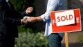 Estate agent and man exchanging money and house keys against sold signboard Royalty Free Stock Photo