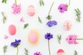 Ester holiday composition with colorful eggs, spring flowers, hypericum and leaves of lavender on white background. Flat lay