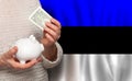 Estonian woman with money bank on the background of Estonia flag. Dotations, pension fund, poverty, wealth, retirement concept