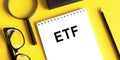 ETF Exchange Traded Funds word written on a notepad next to glasses, a pencil and a magnifying glass on a yellow background Royalty Free Stock Photo