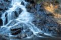 Ethereal long exposure waterfall over black rocks in dappled light. Royalty Free Stock Photo