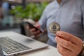 Ethereum coin held in the hand of a trader monitoring the market with his laptop and smartphone