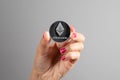 Ethereum silver coin in a woman& x27;s hand over gray background. Blockchain Cryptocurrency. Virtual Money.Crypto currency