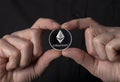 Ethereum silver crypto coin in hands on black background. Eth or etherum close up