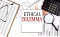 ETHICAL DILEMMA text on notebook with clipboard and calculator on a chart background