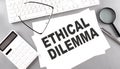 ETHICAL DILEMMA text on paper with keyboard, calculator on grey background