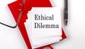 ETHICAL DILEMMA text on sticker on red notebook with pen and glasses