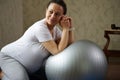 Ethnic adult pregnant woman leaning on a fit ball, smiling looking away while doing prenatal fitness exercises at home Royalty Free Stock Photo