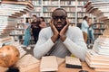Ethnic african american guy surrounded by books in library. Student is bored and tired. Royalty Free Stock Photo