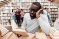 Ethnic african american guy surrounded by books in library. Student is bored and tired. Royalty Free Stock Photo