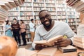 Ethnic african american guy surrounded by books in library. Student is reading book. Royalty Free Stock Photo