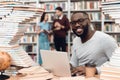 Ethnic african american guy surrounded by books in library. Student is using laptop and drinking coffee. Royalty Free Stock Photo