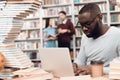 Ethnic african american guy surrounded by books in library. Student is using laptop and drinking coffee. Royalty Free Stock Photo