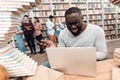 Ethnic african american guy surrounded by books in library. Student is using laptop. Royalty Free Stock Photo