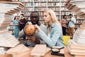 Ethnic african american guy and white girl surrounded by books in library. Students are using globe. Royalty Free Stock Photo