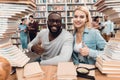 Ethnic african american guy and white girl surrounded by books in library. Students are giving thumbs up. Royalty Free Stock Photo