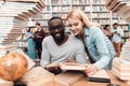Ethnic african american guy and white girl surrounded by books in library. Students are reading book. Royalty Free Stock Photo