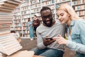 Ethnic african american guy and white girl surrounded by books in library. Students are taking selfie. Royalty Free Stock Photo