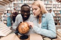 Ethnic african american guy and white girl surrounded by books in library. Students are using globe. Royalty Free Stock Photo