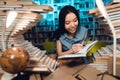 Ethnic asian girl surrounded by books in library. Student is writing in notebook. Royalty Free Stock Photo