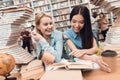 Ethnic asian girl and white girl surrounded by books in library. Students are reading book.