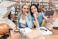 Ethnic asian girl and white girl surrounded by books in library. Students are taking selfie. Royalty Free Stock Photo