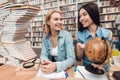 Ethnic asian girl and white girl surrounded by books in library. Students are using globe. Royalty Free Stock Photo