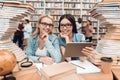 Ethnic asian girl and white girl surrounded by books in library. Students are using tablet. Royalty Free Stock Photo