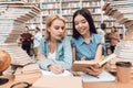 Ethnic asian girl and white girl surrounded by books in library. Students are reading book. Royalty Free Stock Photo