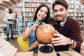 Ethnic asian girl and white guy surrounded by books in library. Students are using globe. Royalty Free Stock Photo