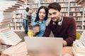 Ethnic asian girl and white guy surrounded by books in library. Students are using laptop. Royalty Free Stock Photo