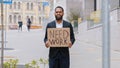 Ethnic bearded frustrated hopeless fired African American man guy worker in city holding poster need work help searching