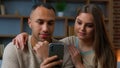 Ethnic couple use mobile phone apps smiling african american man and caucasian woman looking at smartphone screen watch Royalty Free Stock Photo