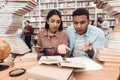 Ethnic indian mixed race girl and guy surrounded by books in library. Students are taking notes. Royalty Free Stock Photo